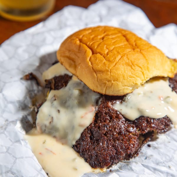 A Burger Nerds burger with a thick patty and creamy cheese sauce on crinkled white paper.