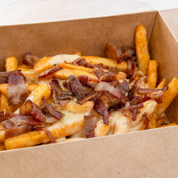 Crispy golden fries topped with melted cheese sauce and generous pieces of bacon in a cardboard box.