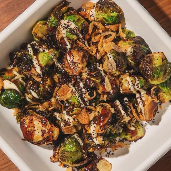 Roasted Brussels sprouts with a dark glaze, white sauce, and crispy fried onions in a white dish.