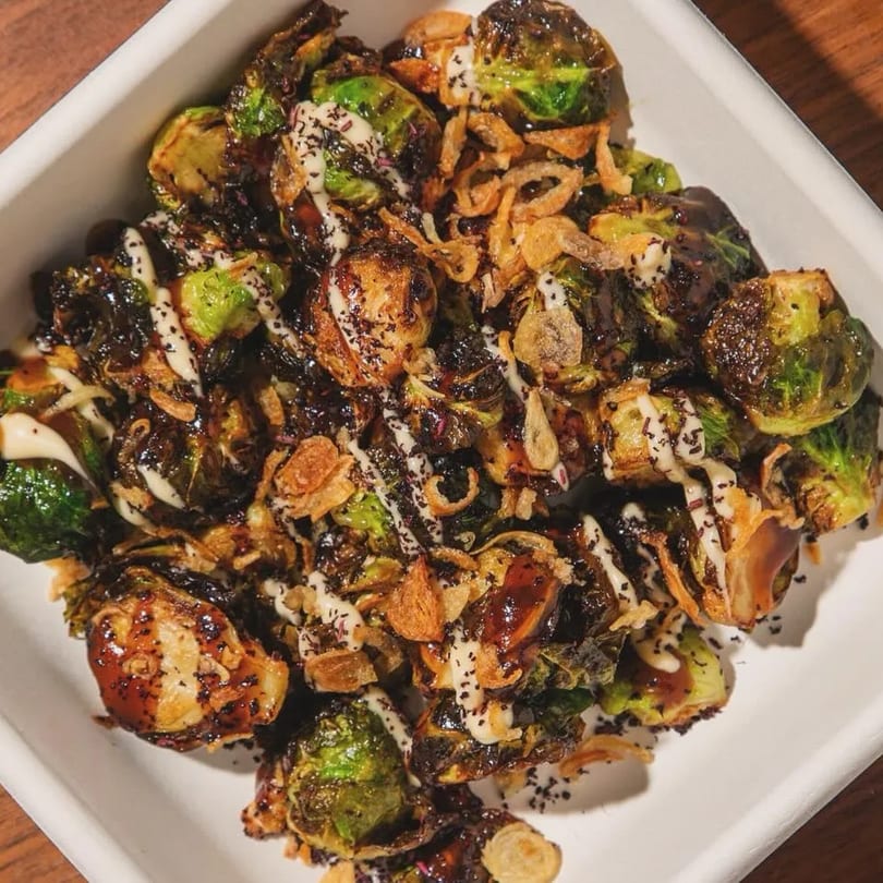 Roasted Brussels sprouts with crispy fried onions, a dark glaze, and white sauce in a white dish.