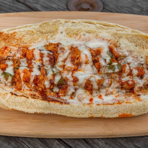 A close-up of a chicken cheesesteak sandwich on a wooden board, filled with chicken, peppers, and melted cheese.
