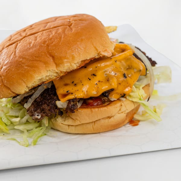 A Burger Nerds burger with melted cheese, shredded lettuce, onions, and a golden bun.